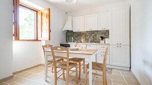 A modern kitchen with white cabinets, a dining table with chairs, and a window with open shutters. - Trullo Bella Vista With Patio & Parking (Locorotondo)