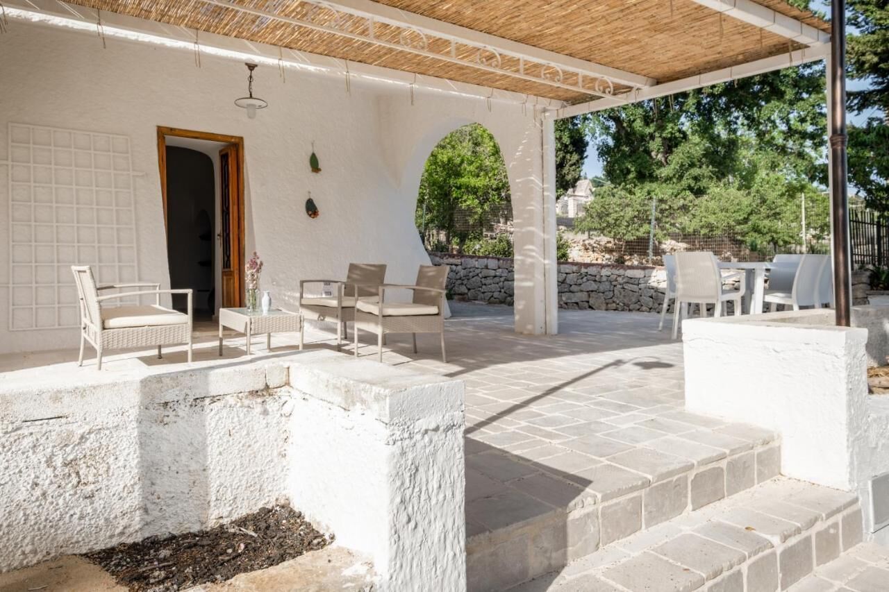 Zona salotto esterna coperta con mobili in vimini bianco e un muro in pietra sullo sfondo.
