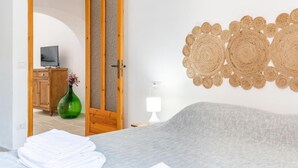 A bedroom with a bed, a wooden door, a television, a cabinet, and a decorative wall hanging. - Trullo Bella Vista With Patio & Parking (Locorotondo)
