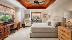 A bedroom with a large bed, a desk, a chair, and a ceiling fan.