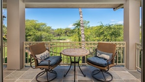 A covered patio with two wicker chairs and a round table, overlooking a lush green landscape.