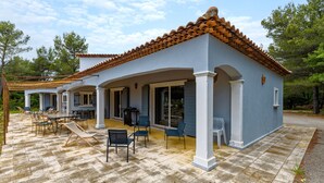 Una casa con techo de tejas, patio exterior con sillas y mesas, y un espacio cubierto con pérgola.