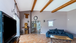 Una sala de estar con televisor, sofá, mesa de centro de madera y suelo de baldosas.