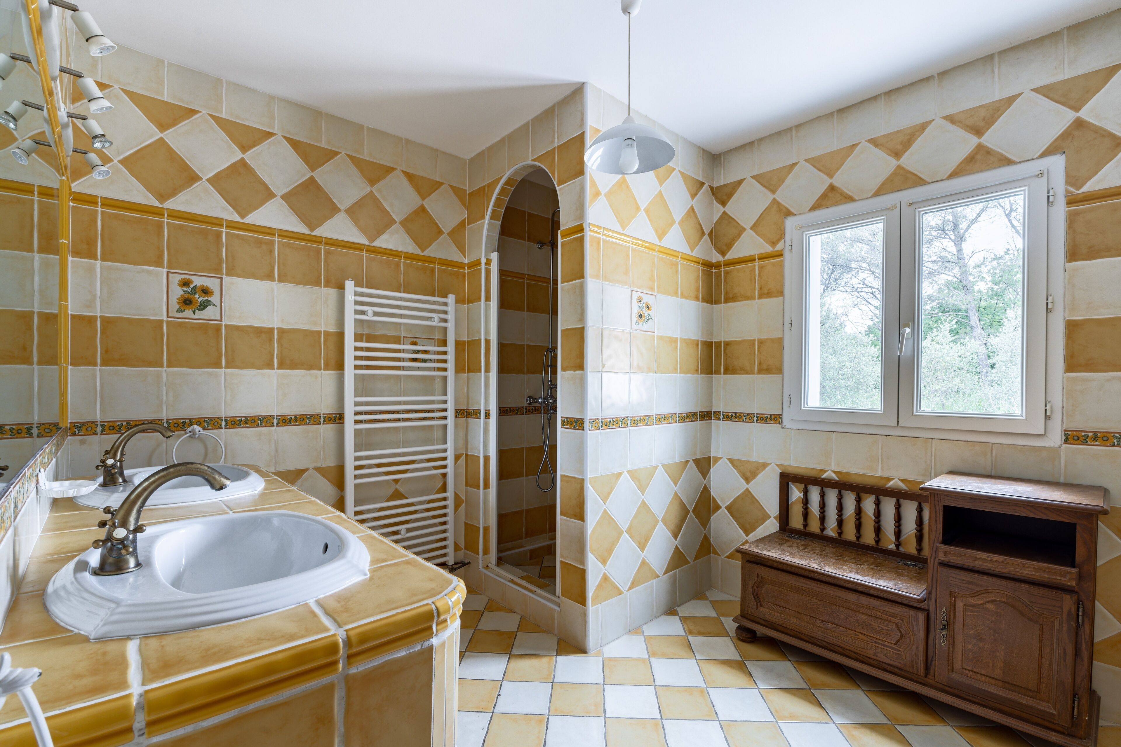 Un baño con lavamanos, espejo, ducha y tocador con ventana.