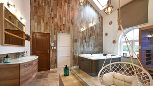 A modern bathroom with a wooden wall, a large mirror, a wooden door, a white bathtub, and a hanging chair. - Instinct - Jacuzzi, Sauna, Apéritif dînatoire et petit déjeuner (Rocquigny)