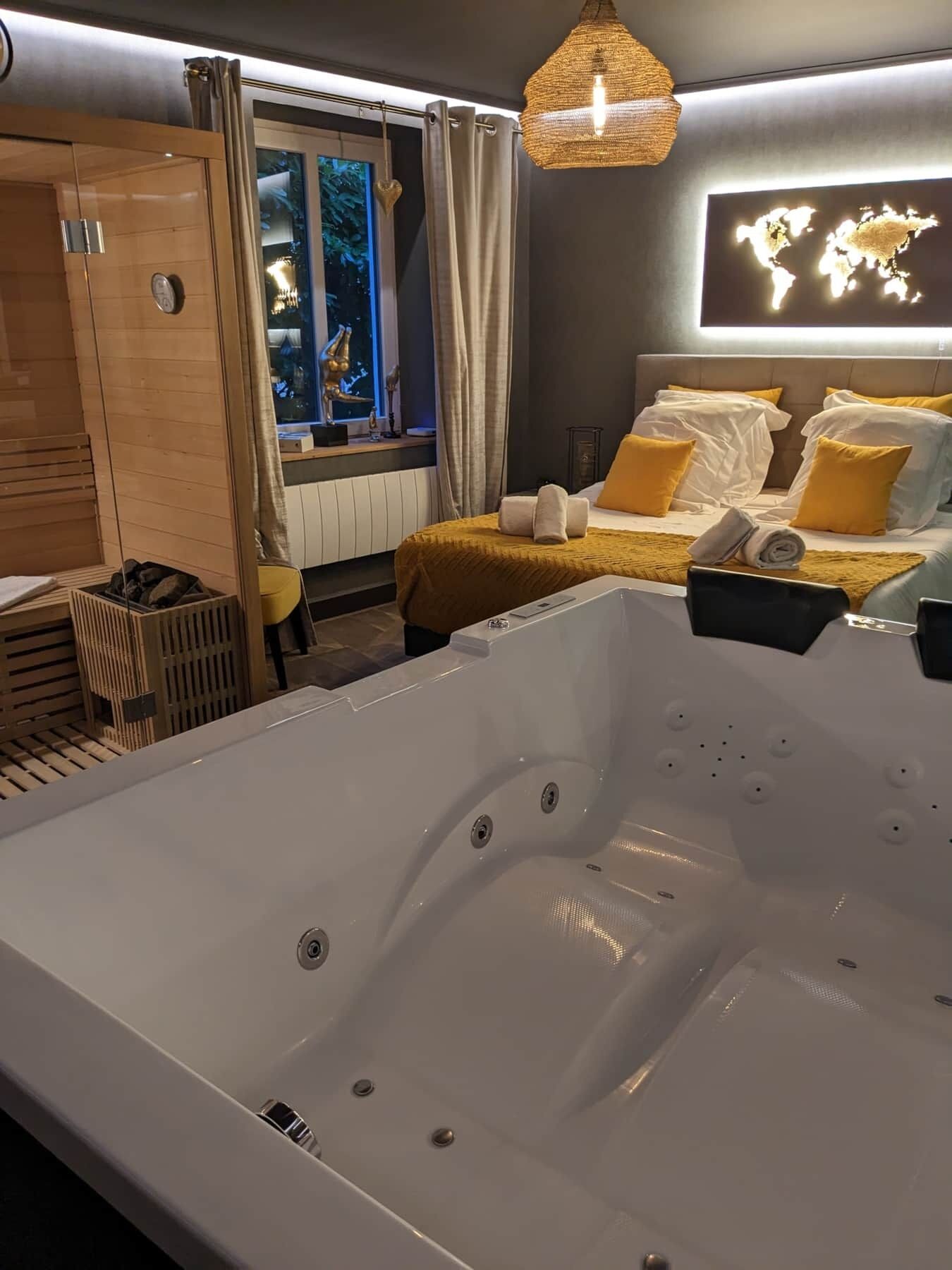Ein modernes Hotelzimmer mit einer großen Badewanne, einem Bett mit gelb-weißer Bettwäsche, Blick ins Freie durch ein Fenster und einer Weltkarte an der Wand.