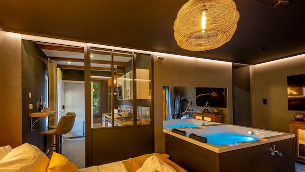 Une chambre d’hôtel moderne avec un grand lit, un petit tabouret, une baignoire et une douche séparée par une paroi en verre.