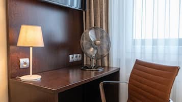 Une chambre d’hôtel équipée d’un bureau, d’une chaise, d’une télévision, d’une lampe et d’un ventilateur.