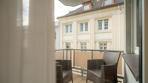 A balcony with wicker chairs, a view of a building with multiple windows, and a tiled floor.