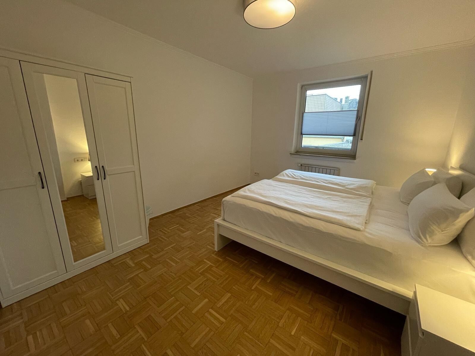 Un dormitorio con cama, armario, ventana y radiador.