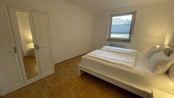 Un dormitorio con cama, armario, ventana y radiador.