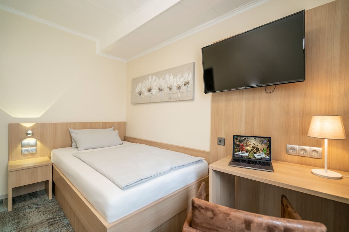 Ein Hotelzimmer mit einem Bett, einem Schreibtisch mit Laptop, einem Fernseher und einem Nachttisch mit Lampe.