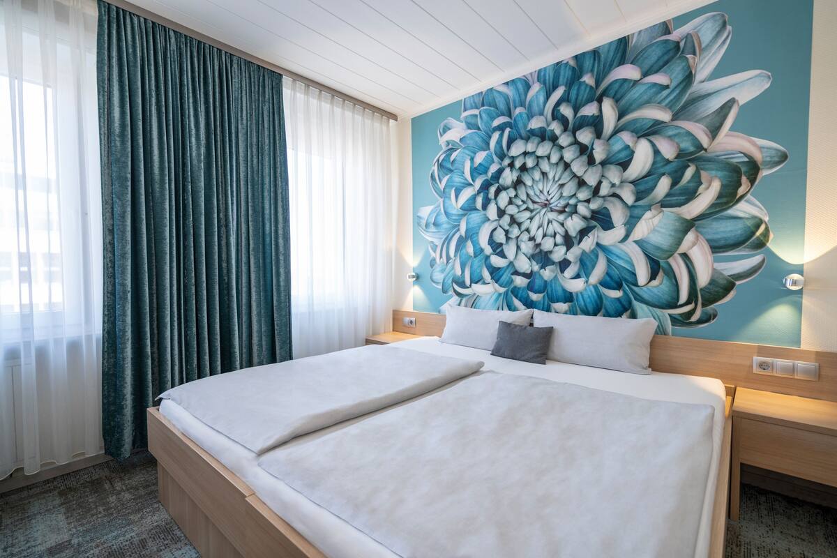 Ein Hotelzimmer mit einem großen Bett, Blick auf die Stadt und einer großen Blumenwand.