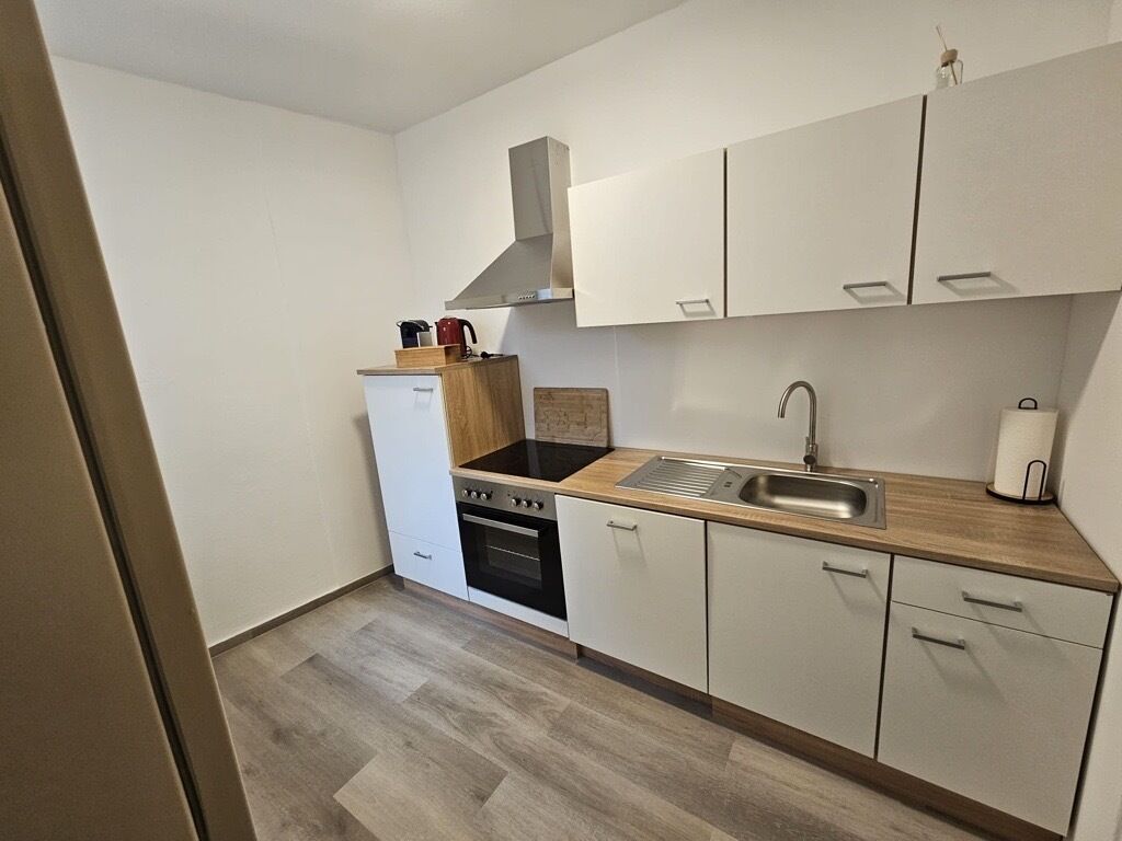 A compact kitchen with white cabinets, a black stove, a sink, and a wooden countertop.