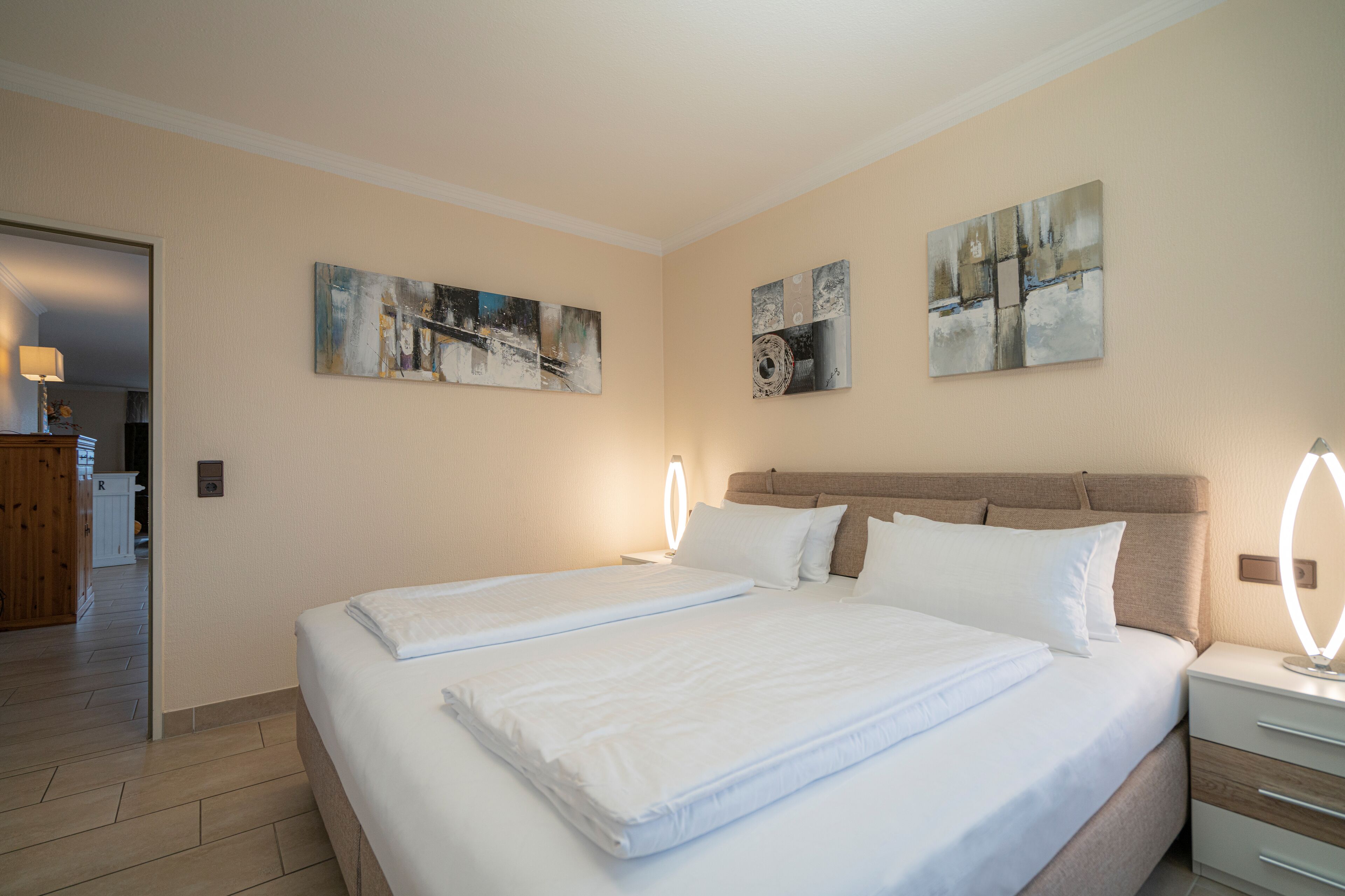 Una habitación de hotel con dos camas, piso de madera y obras de arte en las paredes.
