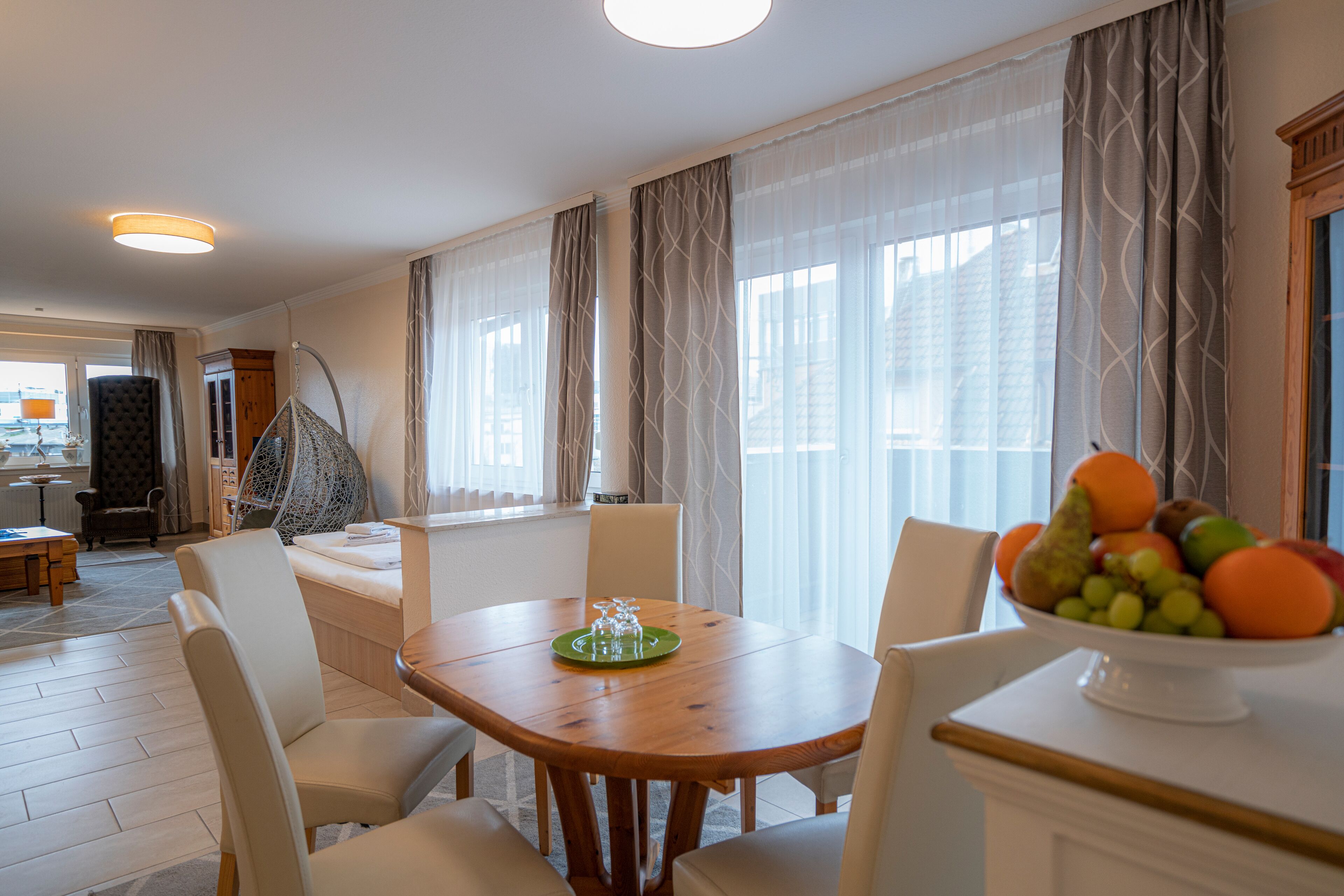 Comedor con una mesa de madera, sillas blancas y un frutero.