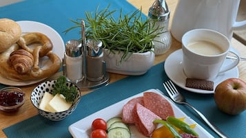 Una mesa de desayuno con croissants, queso, tomates, pepinos, salami y una jarra de leche.