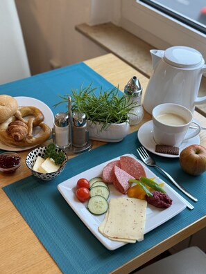 A breakfast table with croissants, cheese, tomatoes, cucumbers, salami, and a pitcher of milk. - Hotel Königshof Dortmund (Dortmund)