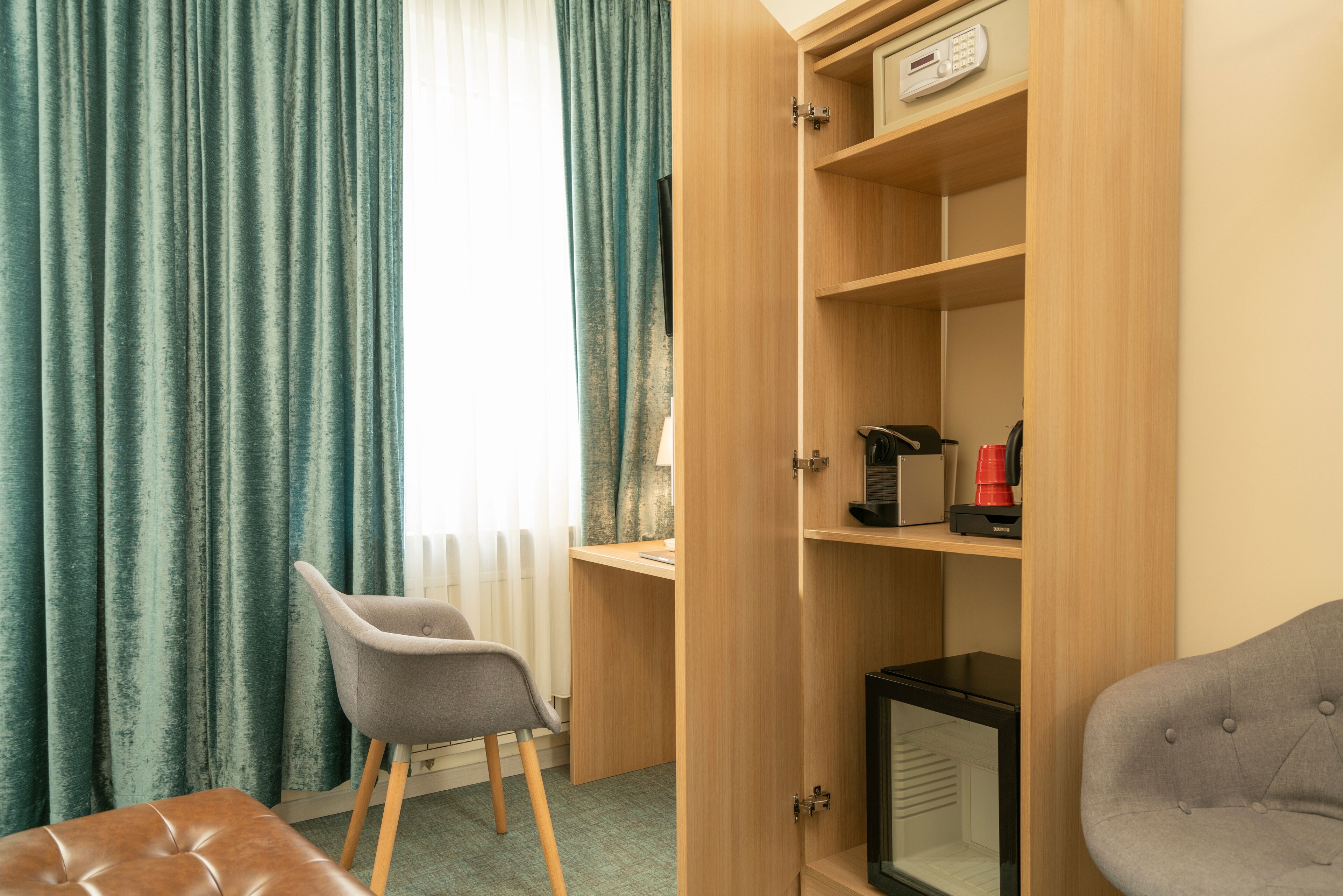Una habitación con un escritorio, una silla, un armario con cafetera y un radiador.
