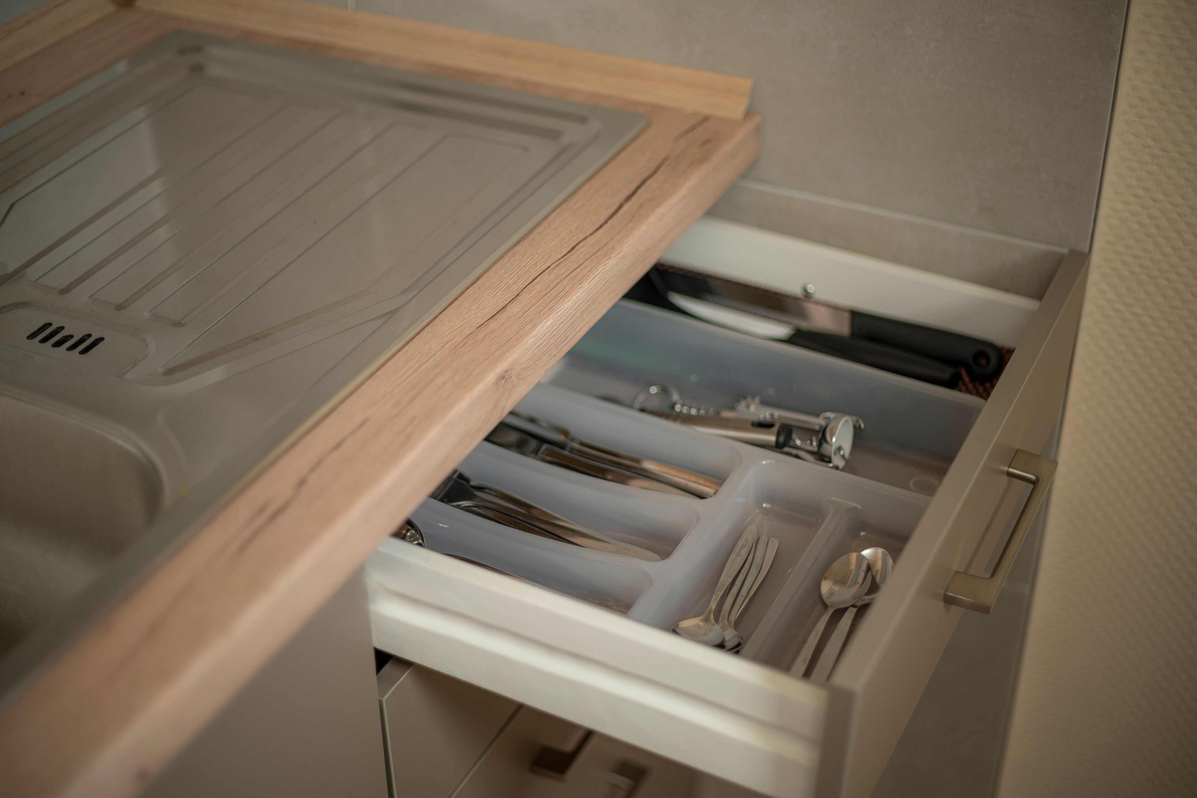 A drawer with utensils and a plastic container.