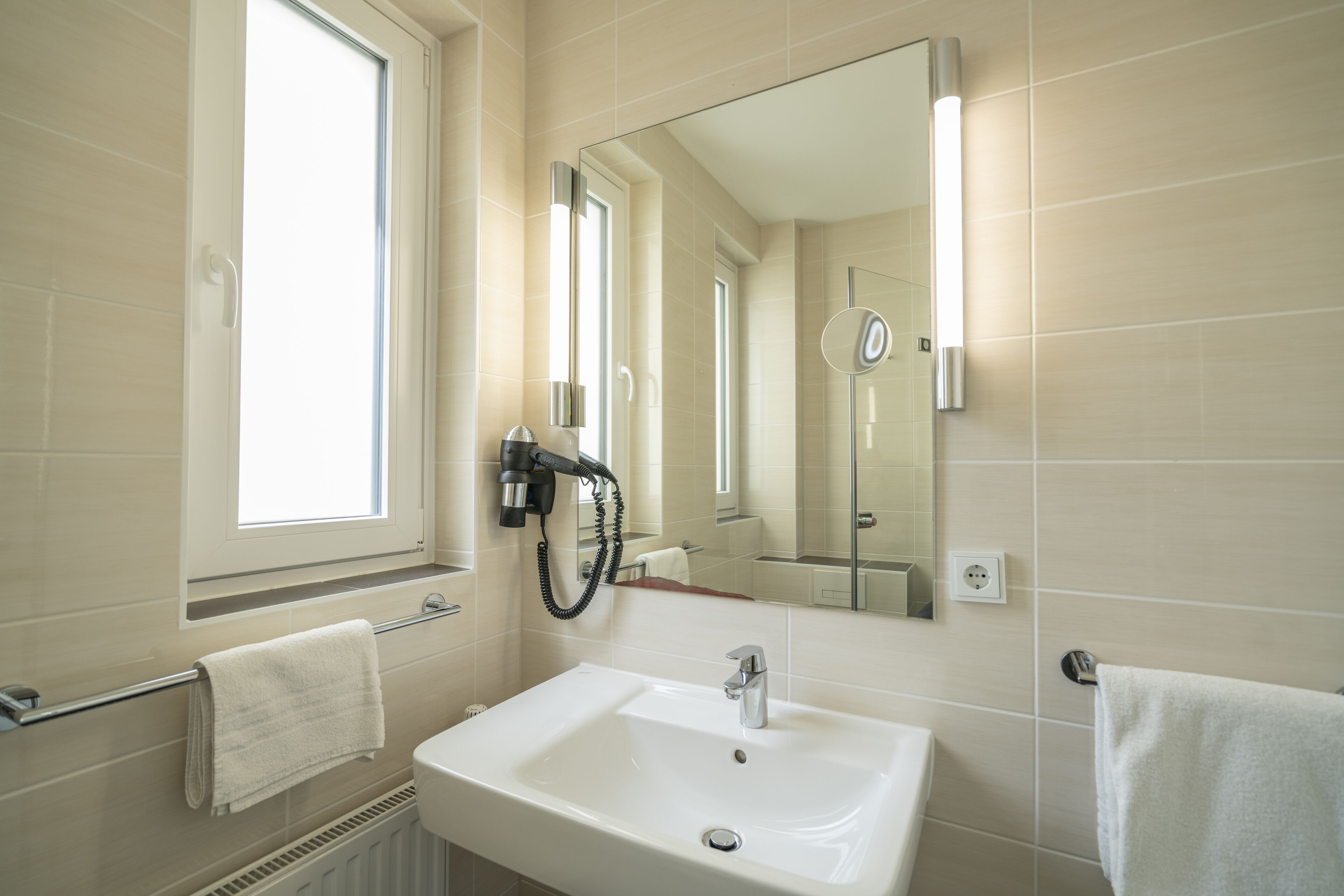 A bathroom with a white sink, a mirror, a towel rack, and a window.