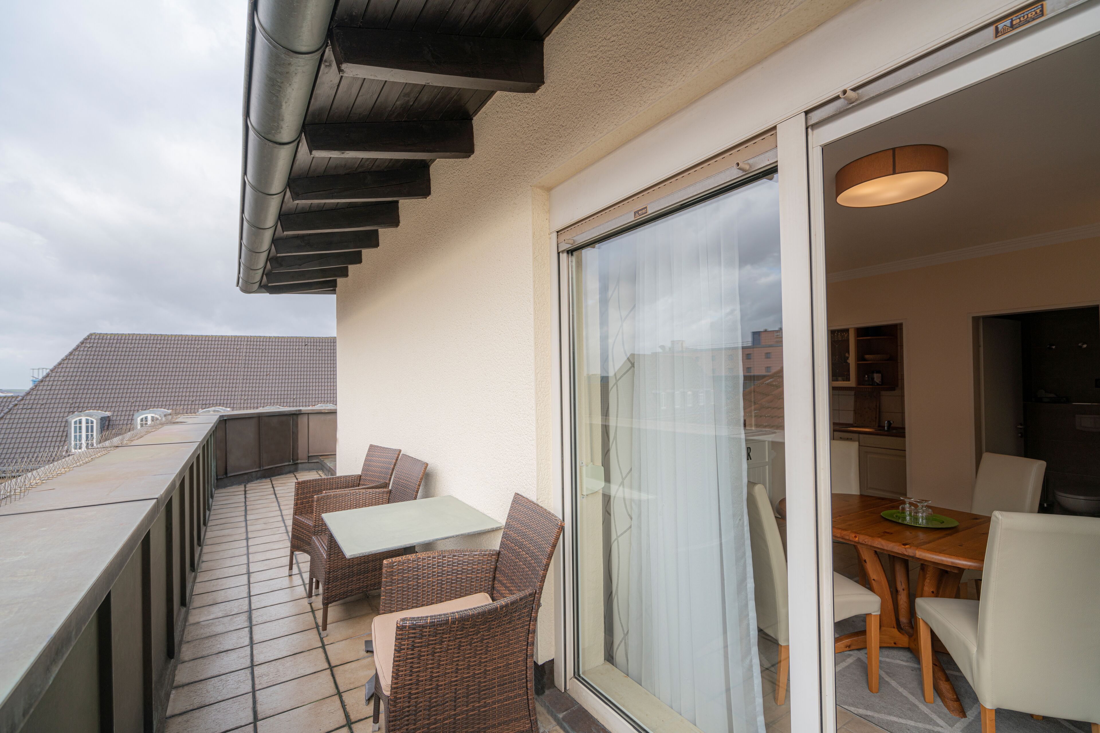 Een balkon met rieten meubilair en een schuifdeur naar een eethoek.