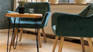 A cozy seating area with two teal chairs and a wooden table, surrounded by potted plants and a tripod-mounted camera.