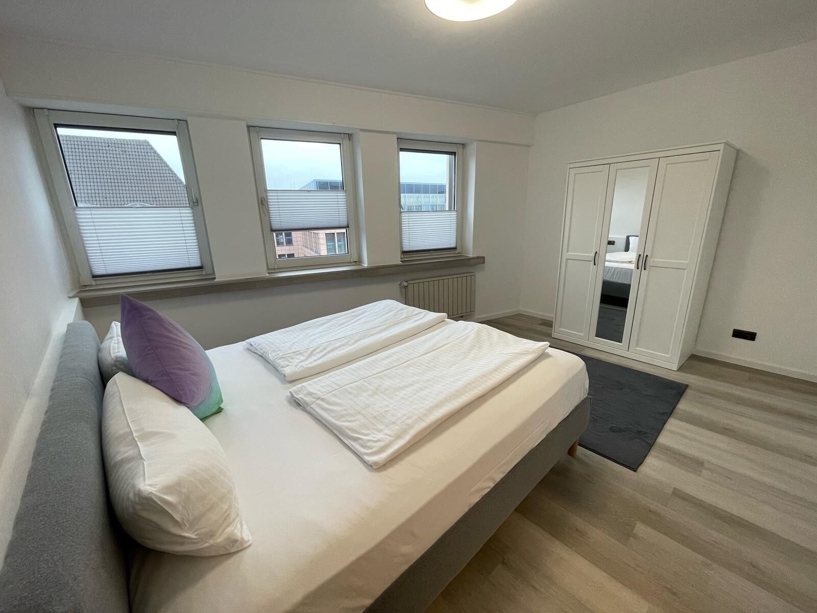 A bedroom with a bed, a wardrobe, and three windows.