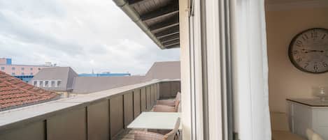 Un balcón con mobiliario de mimbre, un reloj y vistas a edificios.