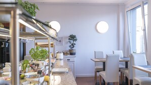 A modern kitchen with a long counter, white cabinets, and a dining area with white chairs and a table.
