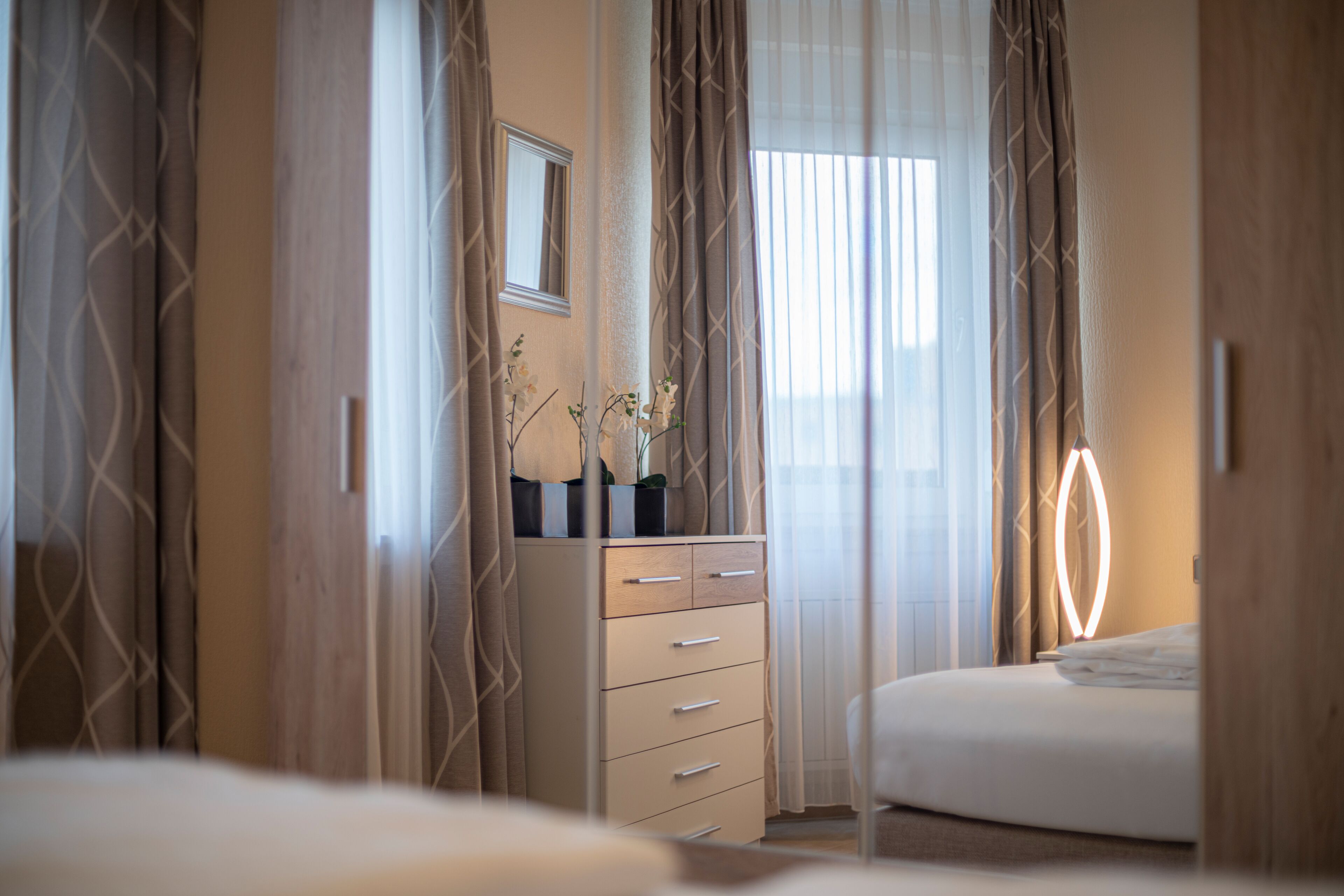 A bedroom with a bed, a dresser, a mirror, and curtains.