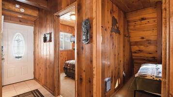 A wooden cabin interior with a door, a bed, a table, and a wall-mounted heater.