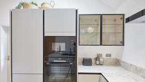 A modern kitchen with a built-in oven, a microwave, and a toaster. There is a glass cabinet above the counter with wine glasses. - Host & Stay | Sunshine Cottage (Leyburn)