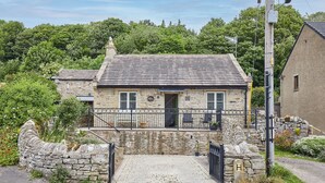 A stone house with a tiled roof, a small porch with chairs, and a stone wall entrance. - Host & Stay | Sunshine Cottage (Leyburn)