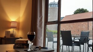 A room with a table, a glass of red wine, and a view of a brick building and a tower through a window. - Coast Cottage -  a very spacious, dog friendly, cottage for 4 guests (Bempton)