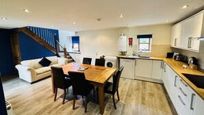 A modern kitchen with a dining area, wooden flooring, and a staircase leading to a blue room. - Coast Cottage -  a very spacious, dog friendly, cottage for 4 guests (Bempton)