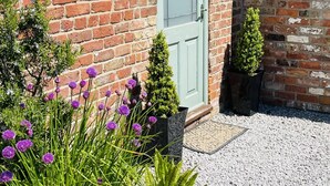 A brick building with a green door, a small garden with purple flowers, and a gravel pathway. - Coast Cottage -  a very spacious, dog friendly, cottage for 4 guests (Bempton)