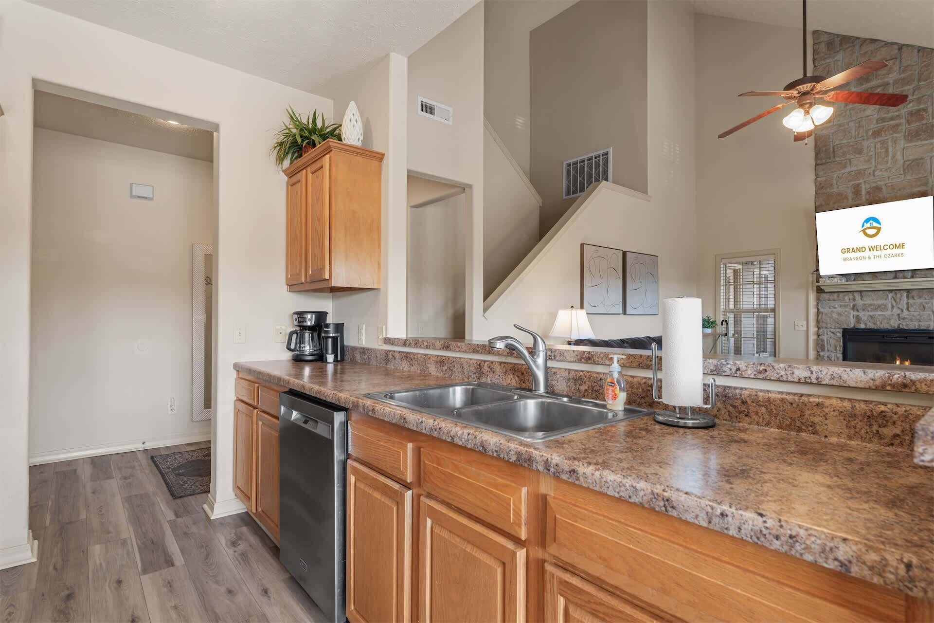 A kitchen with granite countertops, wooden cabinets, a dishwasher, and a stone fireplace.