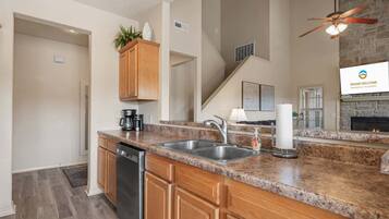 A kitchen with granite countertops, wooden cabinets, a dishwasher, and a stone fireplace.