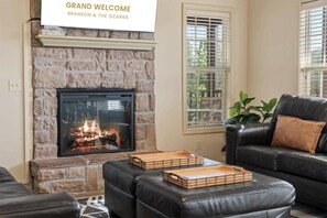 A living room with a stone fireplace, a black leather sofa, and a sign reading 'GRAND WELCOME BRANSON & THE OZARKS'.