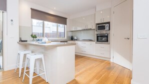 A modern kitchen with a central island, white cabinetry, and stainless steel appliances. - Freda Beach Haven, centrally located (Inverloch)