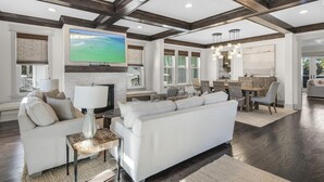 A spacious living room with a large white sofa, a fireplace, and a dining area with a wooden table and chairs. - NatureWalk Community | 6-Seat LSV (Santa Rosa Beach)