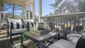 A covered porch with a sofa and chairs, a coffee table, and a view of trees and buildings. - NatureWalk Community | 6-Seat LSV (Santa Rosa Beach)