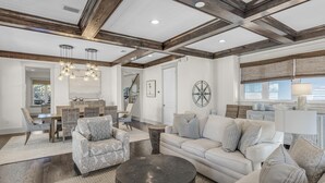 A spacious living room with a high ceiling, exposed wooden beams, a dining area with wicker furniture, and a large wall clock. - NatureWalk Community | 6-Seat LSV (Santa Rosa Beach)