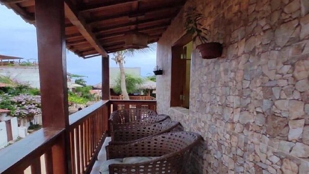 A covered balcony with wicker furniture, stone walls, and a view of the surrounding area.