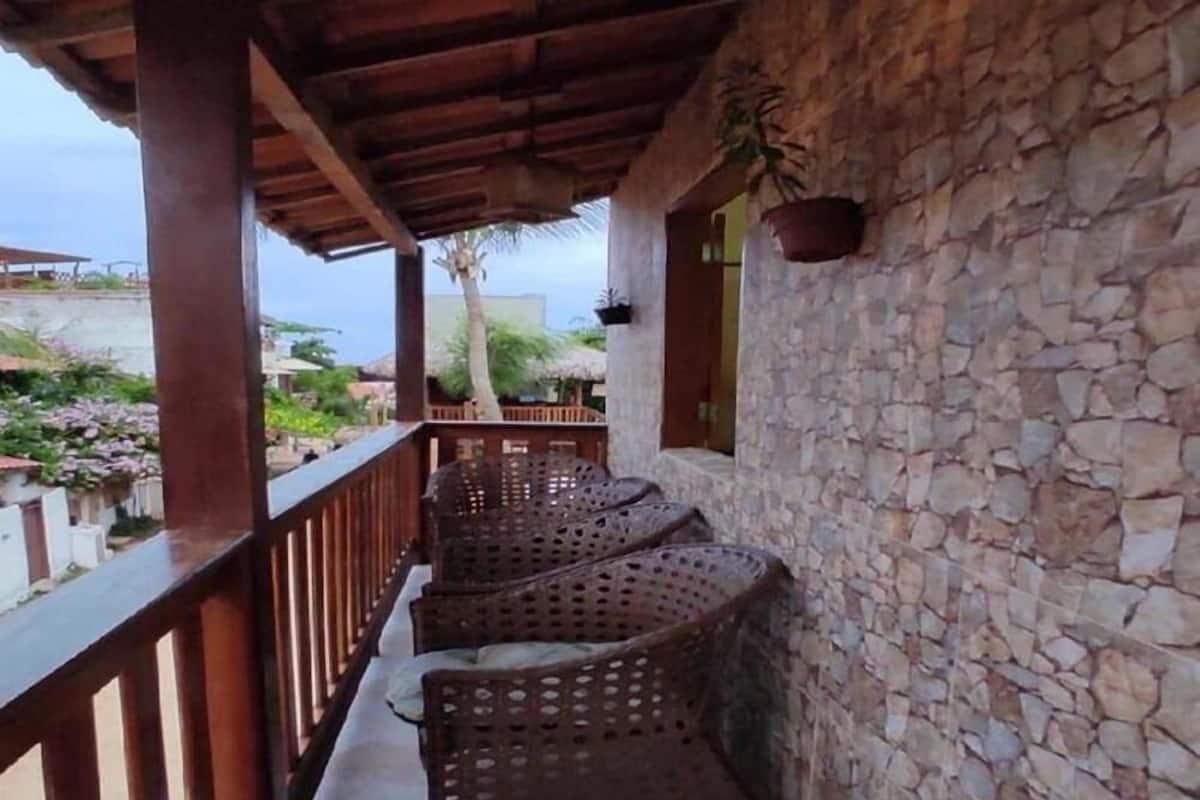 Ein überdachter Balkon mit Korbmöbeln, Steinwänden und Blick auf die Umgebung.