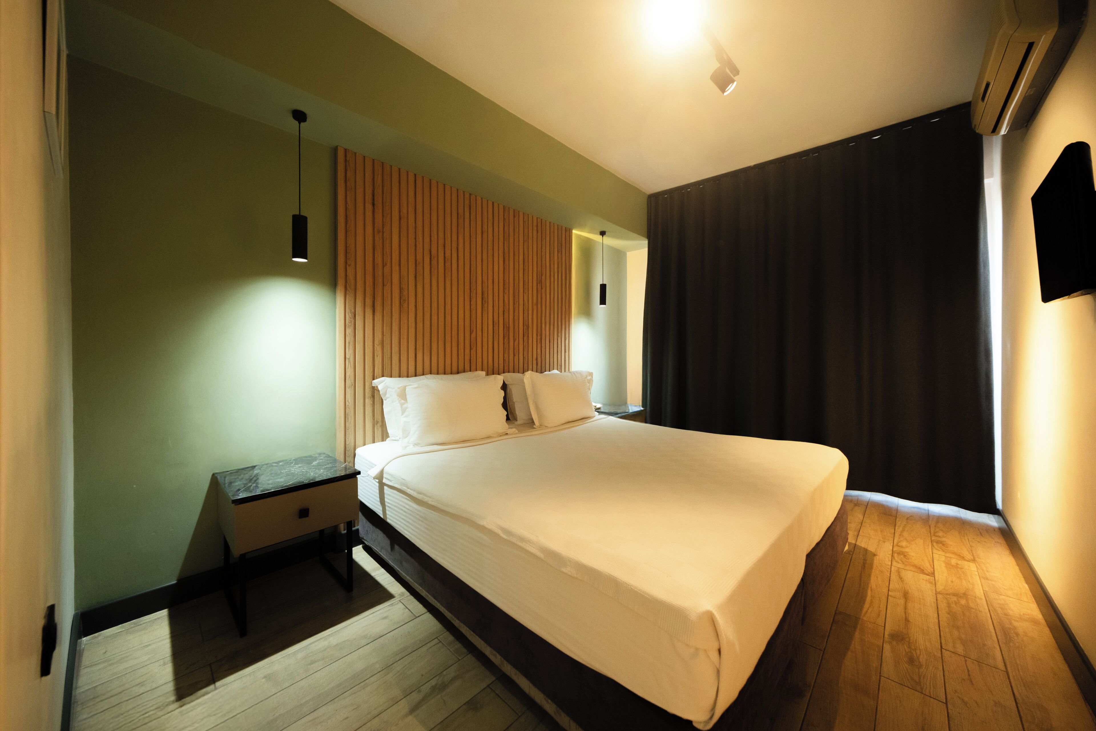 A modern bedroom with a large bed, a nightstand, a wooden headboard, and a wall-mounted TV.