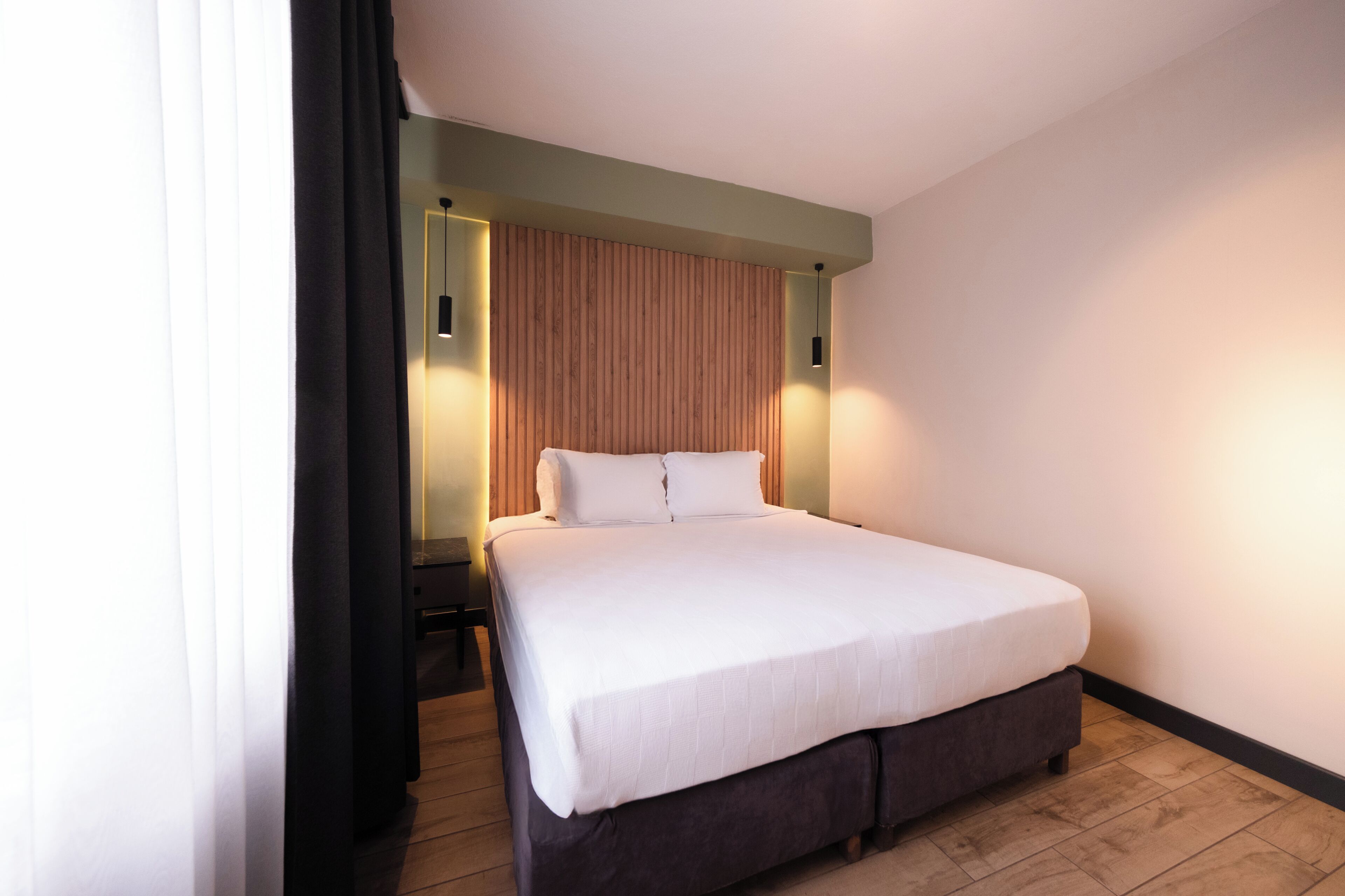 Una habitación de hotel moderna con una cama grande, un panel de madera en la pared y dos lámparas de noche.