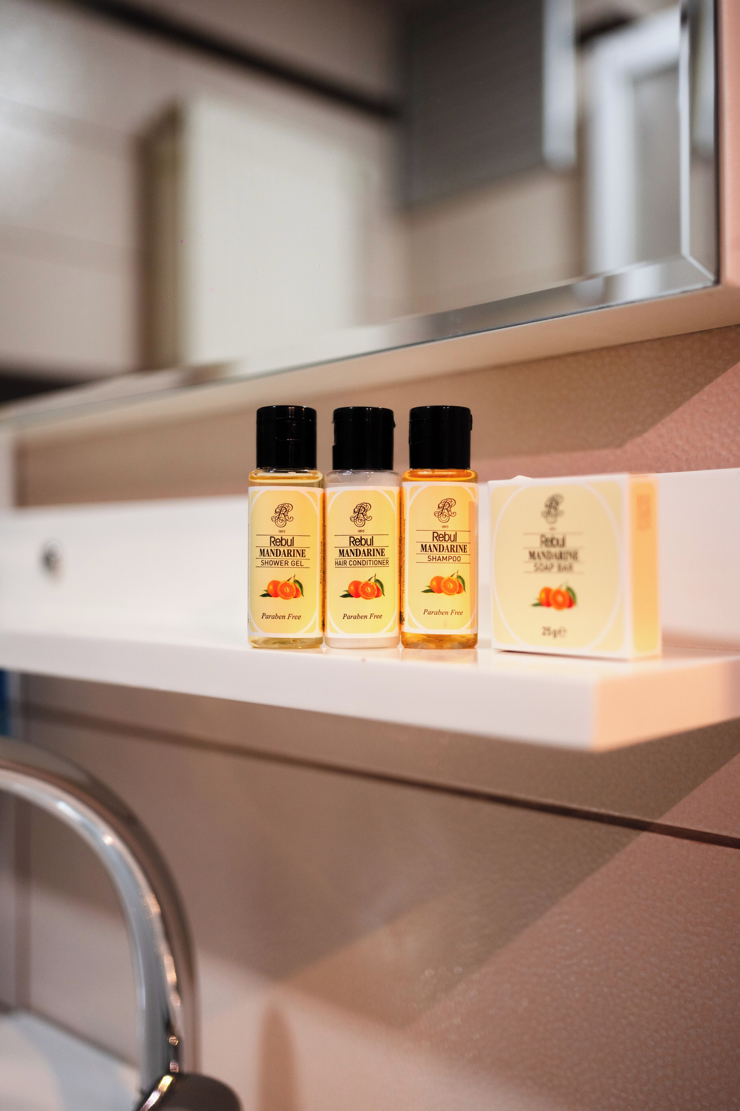 A bathroom shelf with three bottles of Rebul Mandarin shower gel, conditioner, and shampoo, and a bar of soap.