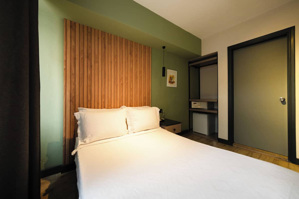 A hotel room with a bed, a wooden headboard, a nightstand, a desk, and a wardrobe.
